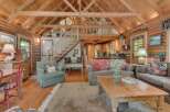 Experience rustic charm in this stunning log cabin living space, featuring a soaring vaulted ceiling with exposed wooden beams and a cozy loft overlooking the main area.