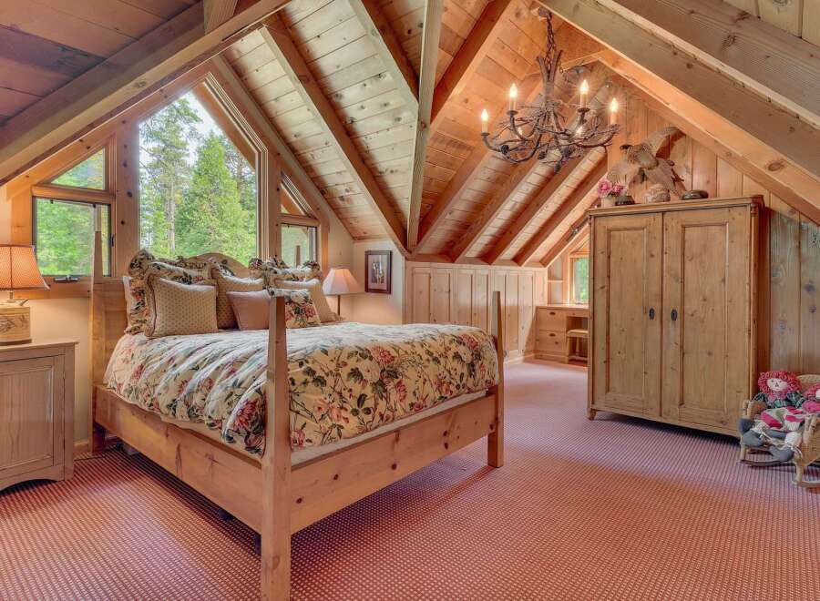 Experience rustic charm in this attic bedroom, featuring a cozy queen-size bed adorned with floral linens and a wooden four-poster frame.