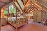 Experience rustic charm in this attic bedroom, featuring a cozy queen-size bed adorned with floral linens and a wooden four-poster frame.