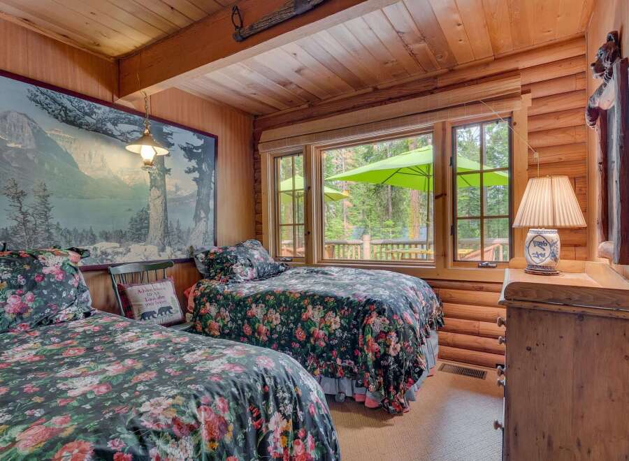 Experience rustic charm in this cozy cabin bedroom featuring two floral-print twin beds and a large scenic mural.