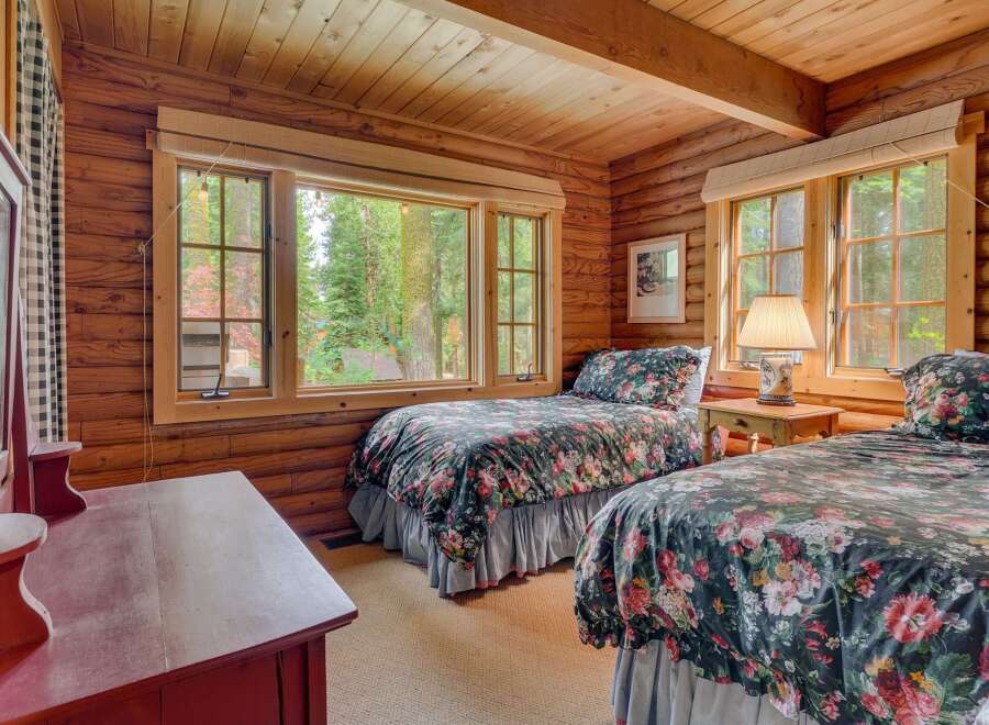 This charming log cabin bedroom features two cozy twin beds adorned with a beautiful floral comforter, perfect for a restful night's sleep.