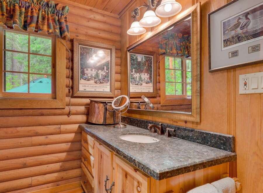 This charming log cabin bathroom features a rustic vanity with a granite countertop and a deep basin sink, perfect for a relaxing getaway.