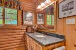 This charming log cabin bathroom features a rustic vanity with a granite countertop and a deep basin sink, perfect for a relaxing getaway.