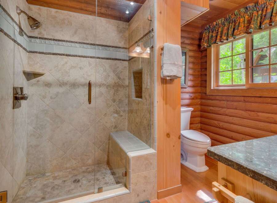Experience rustic charm in this bathroom featuring a spacious glass-enclosed shower with elegant tile work and a built-in bench.