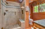 Experience rustic charm in this bathroom featuring a spacious glass-enclosed shower with elegant tile work and a built-in bench.