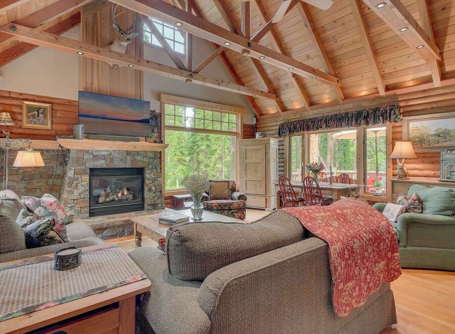 Experience rustic charm in this cozy living room featuring a grand stone fireplace and a vaulted wood-beamed ceiling.