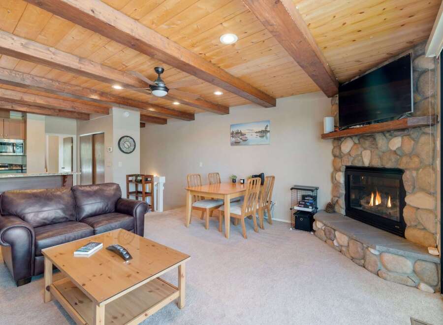Experience cozy living in this charming room featuring a rustic stone fireplace and a warm, wood-beamed ceiling.
