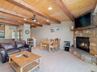 Experience cozy living in this charming room featuring a rustic stone fireplace and a warm, wood-beamed ceiling.