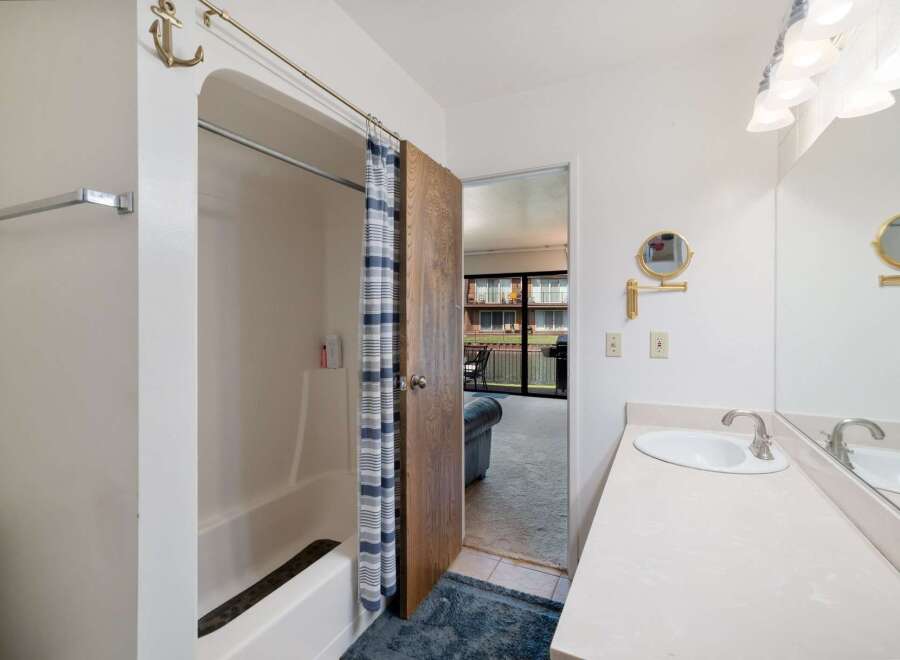 This bathroom features a bathtub with a blue and white striped shower curtain and an anchor-shaped hook.