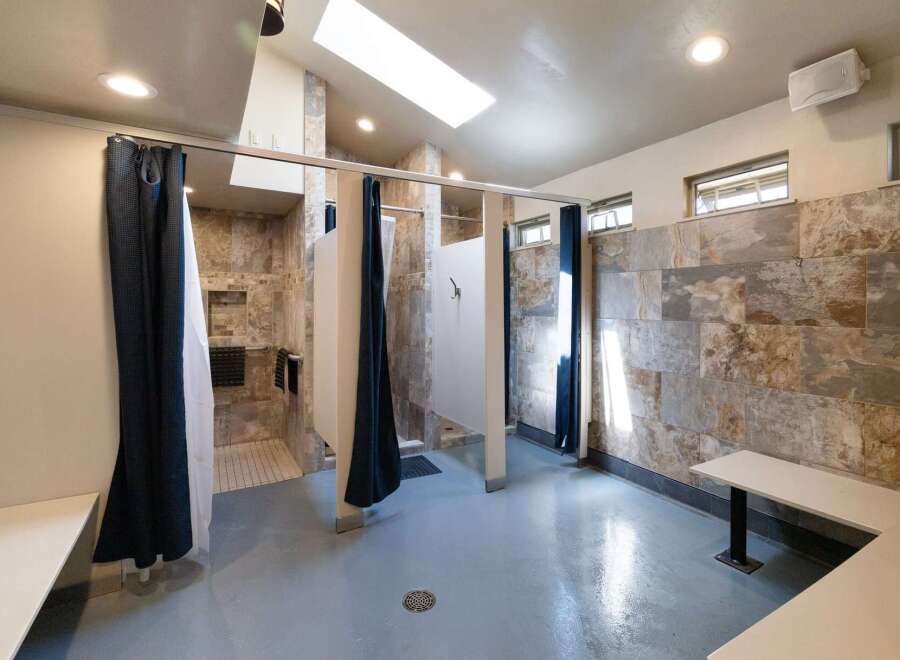 Discover modern comfort in this spacious communal shower facility, featuring private shower stalls with elegant tile work and convenient dark blue curtains.