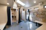 Discover modern comfort in this spacious communal shower facility, featuring private shower stalls with elegant tile work and convenient dark blue curtains.
