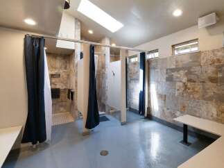 Discover modern comfort in this spacious communal shower facility, featuring private shower stalls with elegant tile work and convenient dark blue curtains.