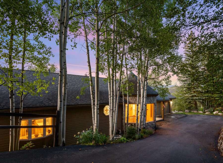 Nestled amongst tall aspen trees, this charming home offers a warm and inviting ambiance, especially as dusk settles.