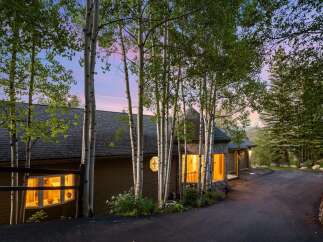 Nestled amongst tall aspen trees, this charming home offers a warm and inviting ambiance, especially as dusk settles.