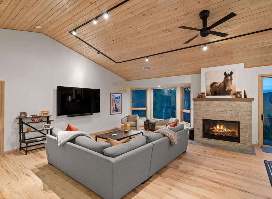 Experience luxurious living in this stunning mountain retreat, featuring a spacious living area with a cozy fireplace and a vaulted wood-paneled ceiling.