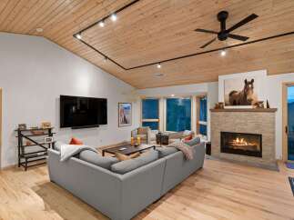 Experience luxurious living in this stunning mountain retreat, featuring a spacious living area with a cozy fireplace and a vaulted wood-paneled ceiling.