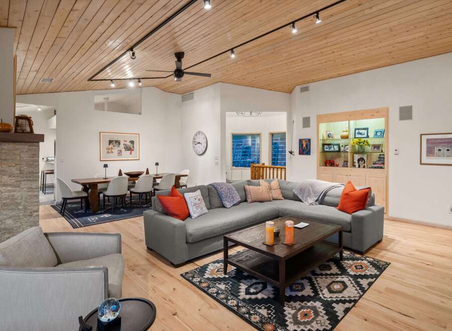 Experience modern living in this spacious open-concept living and dining area, featuring a stunning wood-paneled ceiling and a cozy sectional sofa.