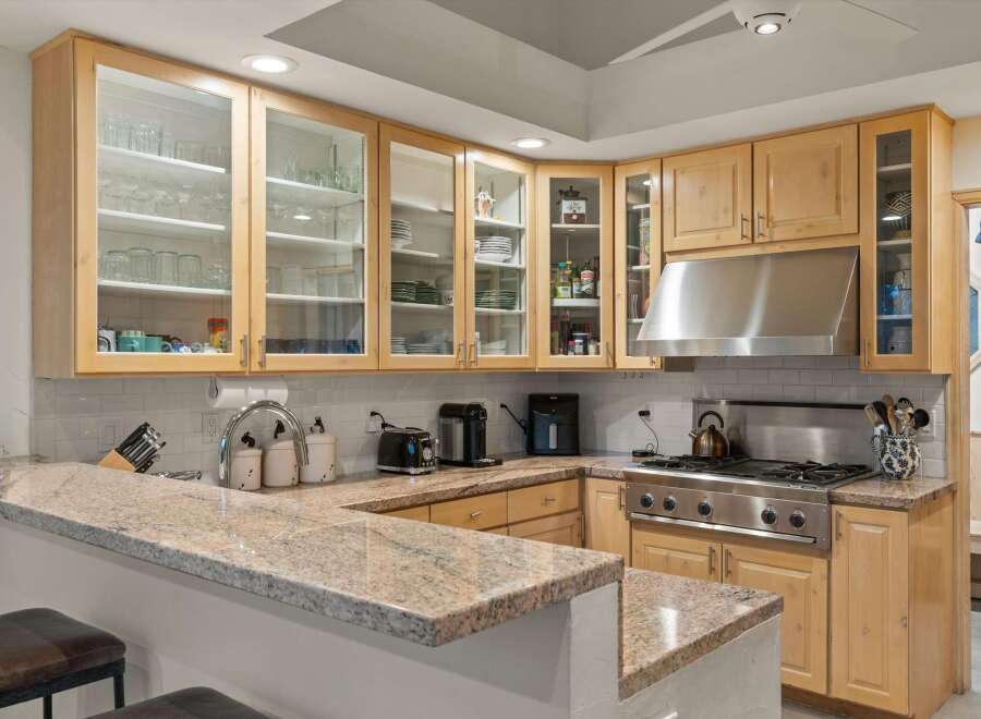 This spacious kitchen boasts beautiful light wood cabinetry with glass-front upper cabinets, perfect for displaying dishware.