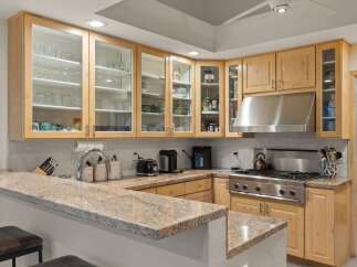 This spacious kitchen boasts beautiful light wood cabinetry with glass-front upper cabinets, perfect for displaying dishware.