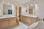 This spacious bathroom features dual vanities with light wood cabinetry and white countertops, offering ample storage and a clean aesthetic.
