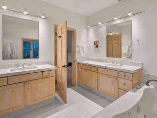 This spacious bathroom features dual vanities with light wood cabinetry and white countertops, offering ample storage and a clean aesthetic.