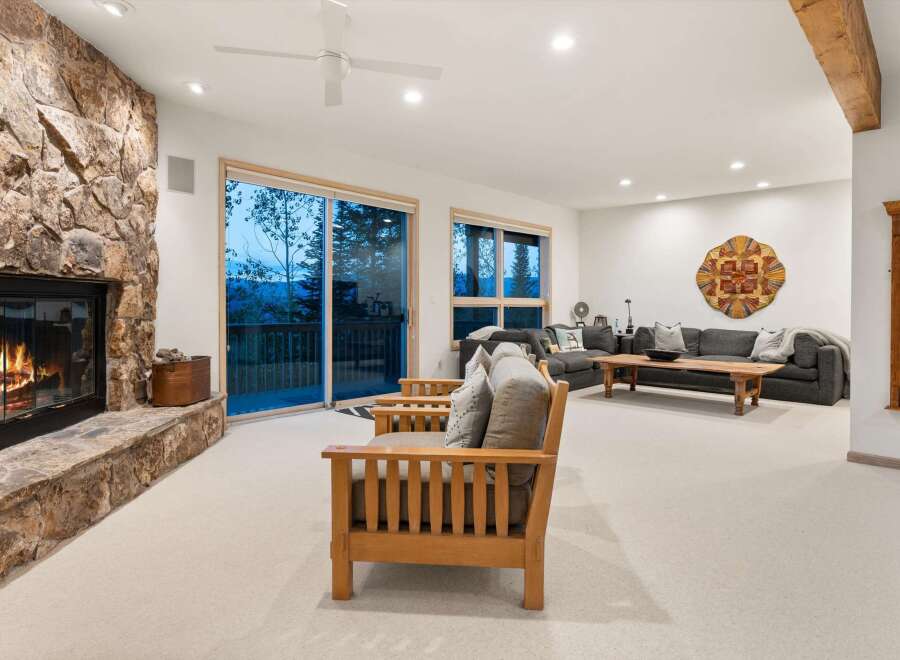 Experience breathtaking mountain views from this stunning living room, featuring a grand stone fireplace and expansive sliding glass doors that open to a scenic deck.