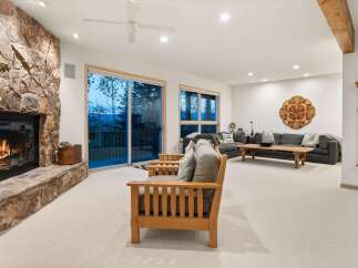 Experience breathtaking mountain views from this stunning living room, featuring a grand stone fireplace and expansive sliding glass doors that open to a scenic deck.