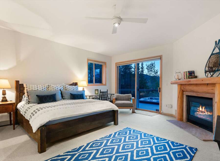 Experience ultimate relaxation in this cozy mountain bedroom, featuring a warm fireplace and a private deck with a hot tub overlooking stunning natural scenery.