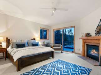 Experience ultimate relaxation in this cozy mountain bedroom, featuring a warm fireplace and a private deck with a hot tub overlooking stunning natural scenery.
