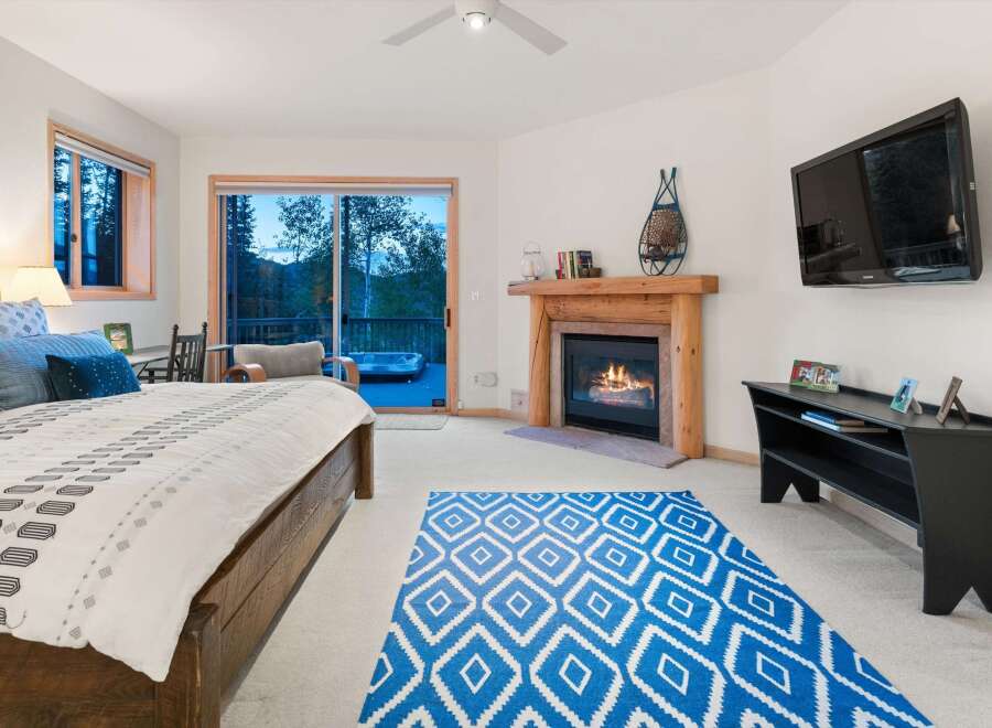 Experience ultimate relaxation in this luxurious bedroom featuring a cozy fireplace and a private balcony with a hot tub overlooking a serene forest.