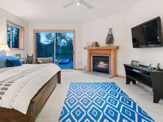 Experience ultimate relaxation in this luxurious bedroom featuring a cozy fireplace and a private balcony with a hot tub overlooking a serene forest.