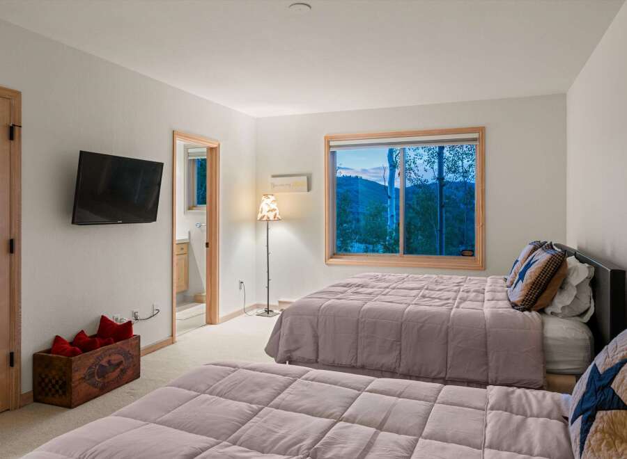 Experience serene mountain living in this charming bedroom featuring two comfortable beds and a large window with breathtaking views of the surrounding landscape.