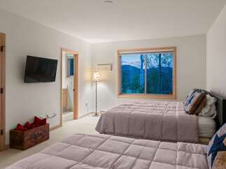 Experience serene mountain living in this charming bedroom featuring two comfortable beds and a large window with breathtaking views of the surrounding landscape.
