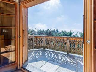 Step out onto this charming balcony with its intricate wooden railing, offering a picturesque view of the surrounding greenery and distant mountains.