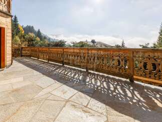 Experience breathtaking mountain views from this stunning balcony, featuring intricate wooden railings and a spacious stone patio.