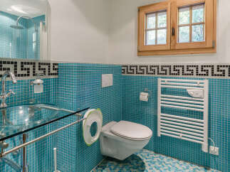 This modern bathroom features vibrant turquoise mosaic tiles throughout, complemented by a sleek glass sink and chrome fixtures.