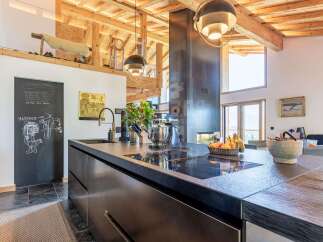 Experience luxury mountain living in this stunning kitchen, featuring a sleek, modern island with integrated stovetop and a striking metallic chimney.