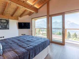 Experience breathtaking mountain views from this luxurious bedroom, featuring a vaulted wooden beam ceiling and expansive windows.