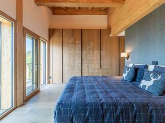 Experience rustic luxury in this stunning bedroom featuring exposed wooden beams and floor-to-ceiling windows that offer breathtaking views.