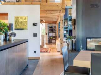 Experience modern alpine living in this stunning open-plan space, featuring exposed wooden beams and a sleek, contemporary kitchen.