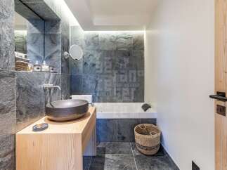 Experience luxury in this modern bathroom featuring a striking stone-tiled accent wall and a sleek wooden vanity.