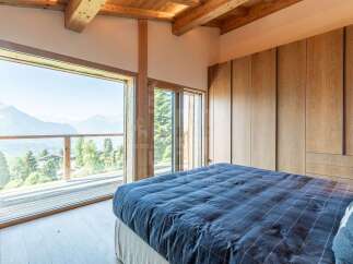 Experience breathtaking mountain views from this serene bedroom, featuring expansive floor-to-ceiling windows that open onto a private deck.
