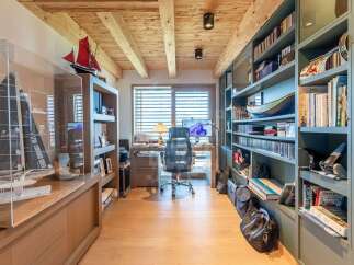 Discover this sophisticated home office featuring a stunning wooden beam ceiling and a wall of built-in bookshelves.
