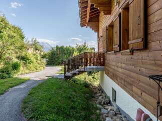 Nestled amidst lush greenery and offering stunning mountain views, this charming wooden chalet boasts a rustic exterior with traditional shutters.