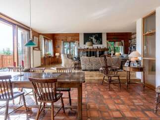 Experience rustic charm in this spacious living and dining area, featuring a large wooden dining table with chairs and a cozy living room with a stone fireplace.