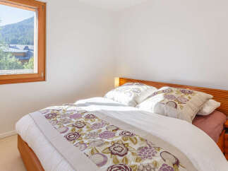 Experience serene mountain living in this charming bedroom, featuring a comfortable bed adorned with floral linens and a picturesque window offering stunning views of the surrounding landscape.