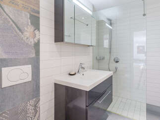 This modern bathroom features a sleek vanity with a white countertop and dark gray drawers, complemented by a chrome faucet.