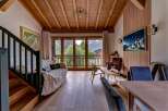 Experience mountain living in this stunning chalet-style living room, featuring a cozy sofa, a modern TV, and breathtaking views from the large glass doors.