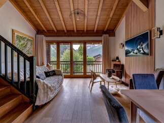 Experience mountain living in this stunning chalet-style living room, featuring a cozy sofa, a modern TV, and breathtaking views from the large glass doors.