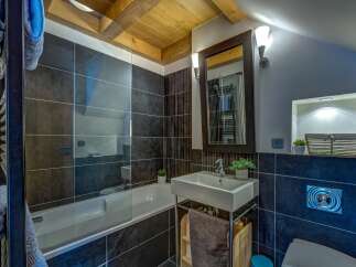 This modern bathroom features a sleek bathtub with a glass enclosure, complemented by dark tiled walls and a wooden ceiling.